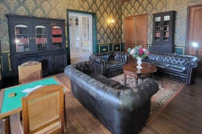 Salon ancien avec parquet en bois, mobilier classique, cheminée, miroir, coiffeuse et grande fenêtre avec rideaux roses.