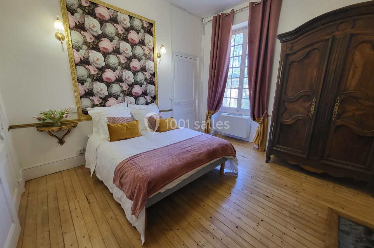 Chambre lumineuse avec lit double, couvre-lit rose, armoire en bois, rideaux assortis et décoration florale au mur.