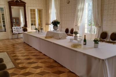 Salon ancien avec parquet en bois, mobilier classique, cheminée, miroir, coiffeuse et grande fenêtre avec rideaux roses.