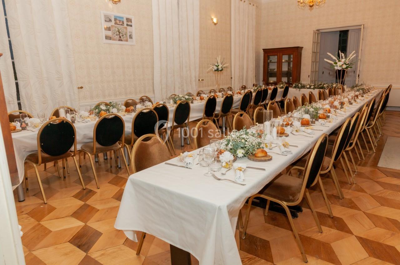 Salle de réception avec deux longues tables dressées, décorées de fleurs blanches et d'éléments naturels.