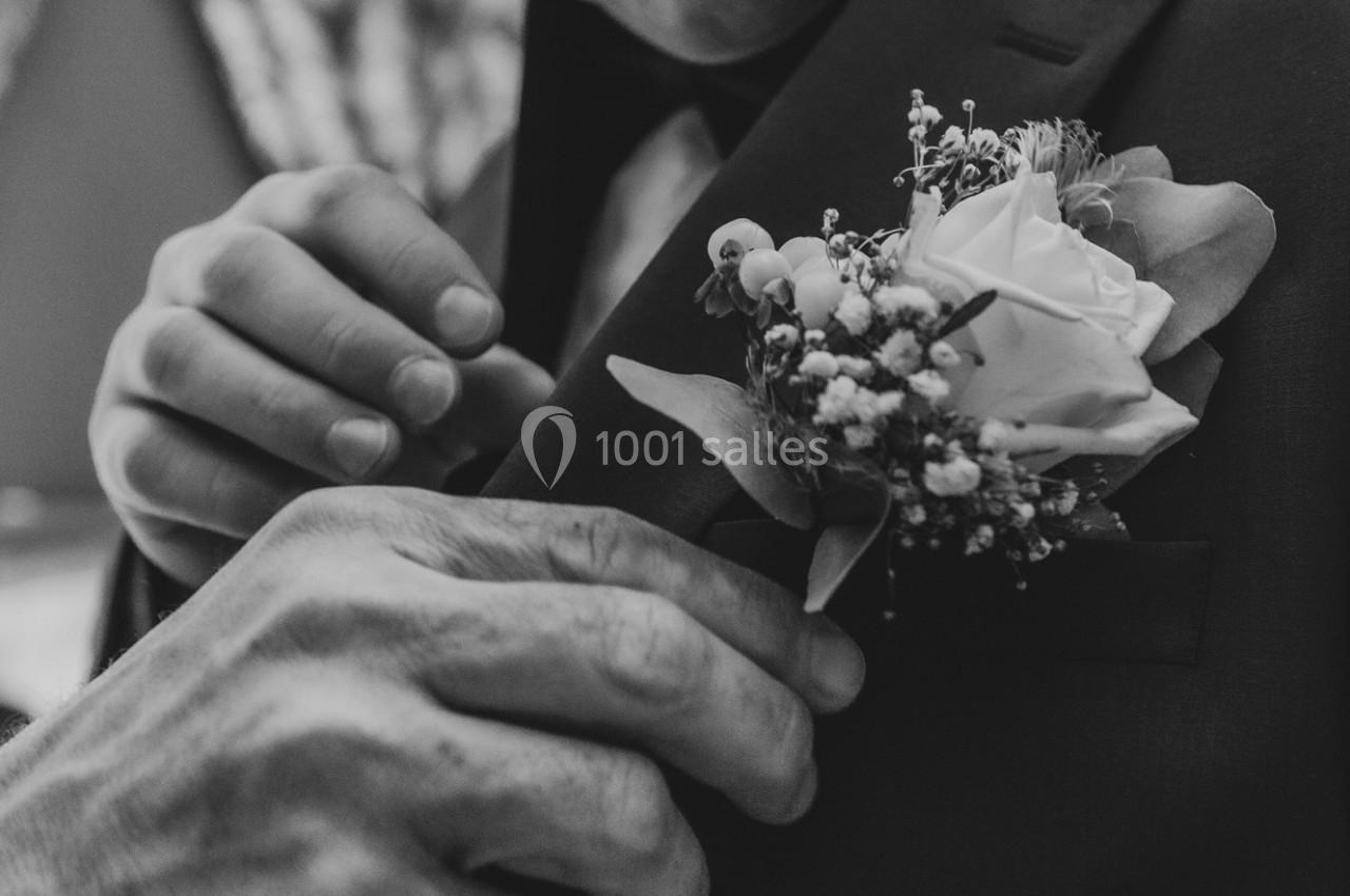 Un homme ajuste une boutonnière composée d'une rose et de petites fleurs blanches sur une veste sombre.