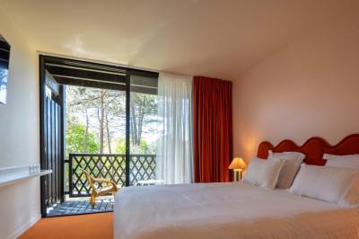 Chambre lumineuse avec lit double, rideaux rouges, balcon donnant sur un espace vert et mobilier minimaliste.