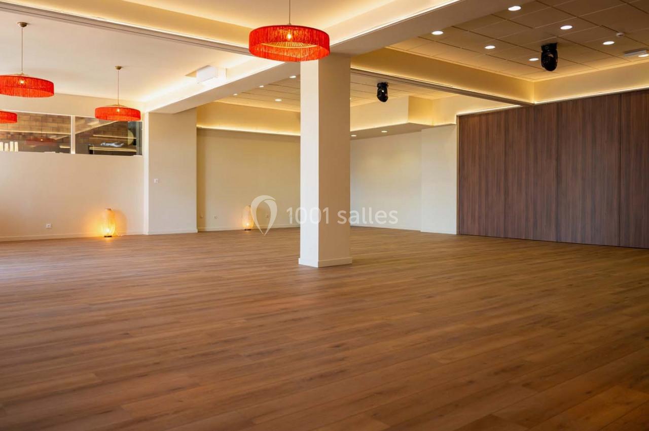 Salle spacieuse avec parquet en bois, murs clairs, éclairage suspendu et panneaux en bois sombre.