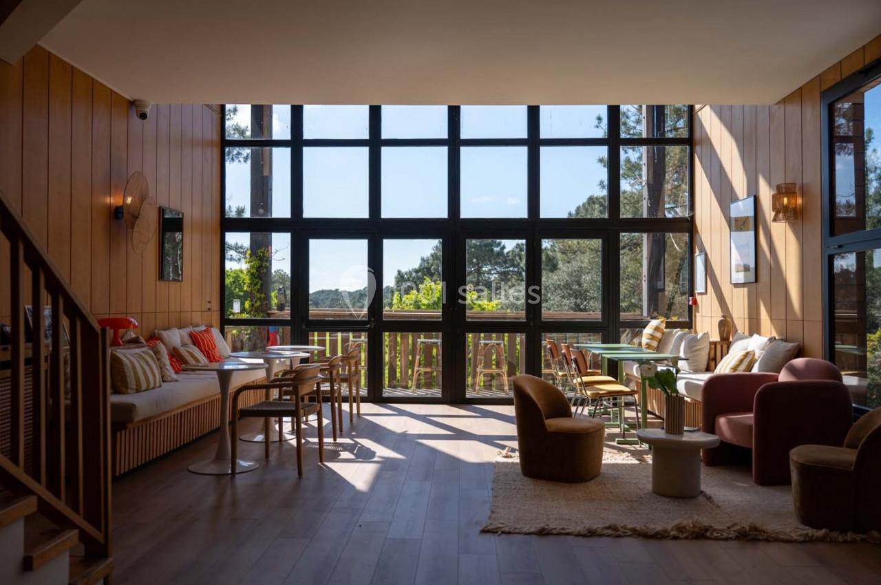 Salon lumineux avec de grandes baies vitrées, mobilier moderne et vue sur un paysage arboré.