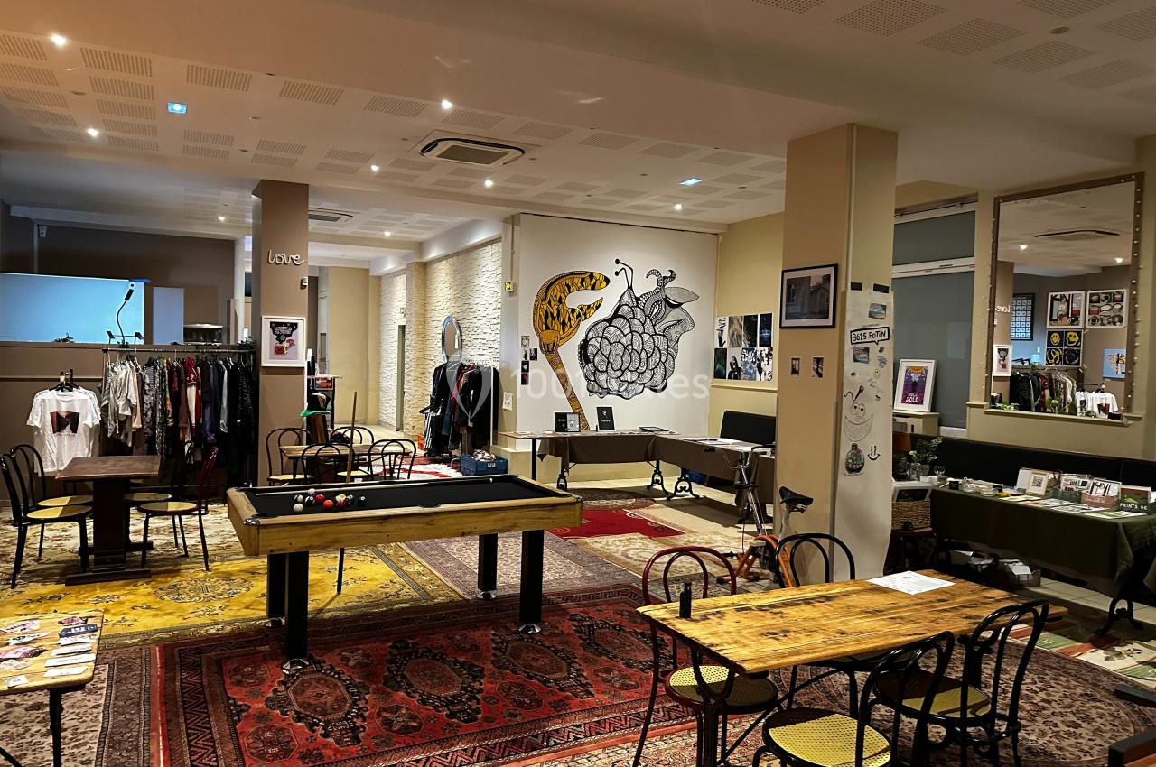 Salle aménagée avec des tables, un billard, des vêtements exposés et des œuvres d'art accrochées aux murs.