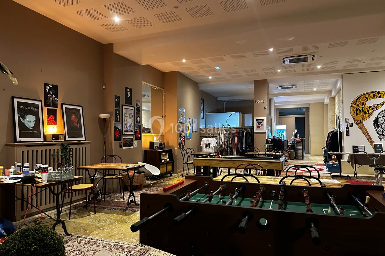 Salle aménagée avec des tables, un baby-foot, des affiches aux murs et des vêtements exposés en arrière-plan.
