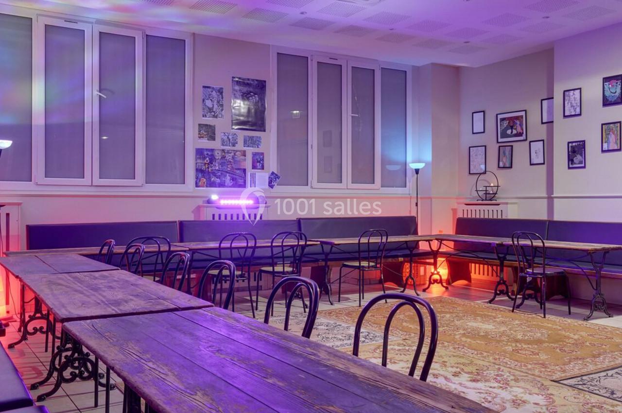 Salle lumineuse avec tables en bois, chaises noires, murs décorés de cadres et éclairage coloré.