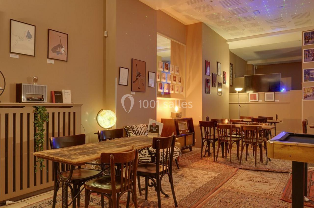 Salle chaleureuse avec tables en bois, chaises anciennes, décorations murales et éclairage tamisé.