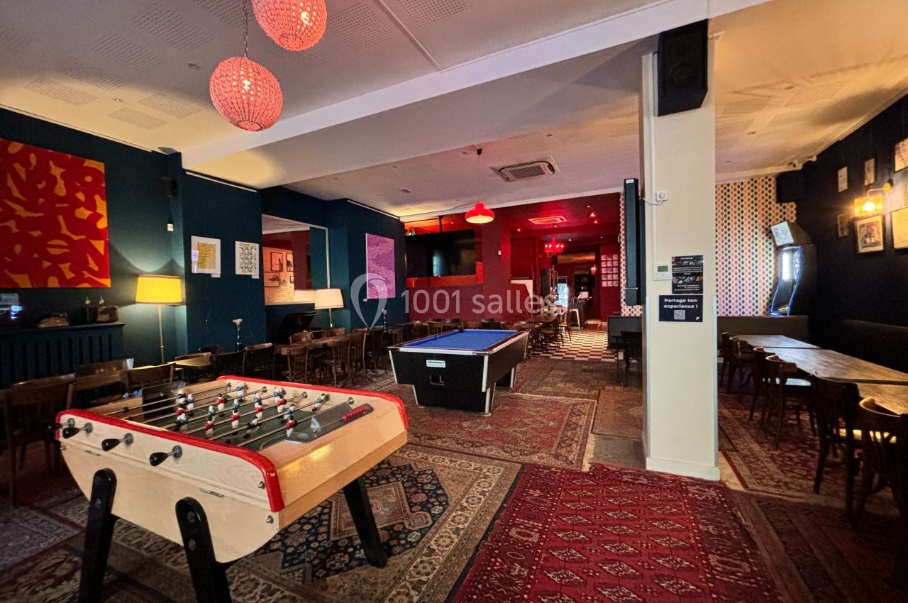Salle de loisirs avec baby-foot, billard, tables en bois et éclairage tamisé dans une ambiance chaleureuse.