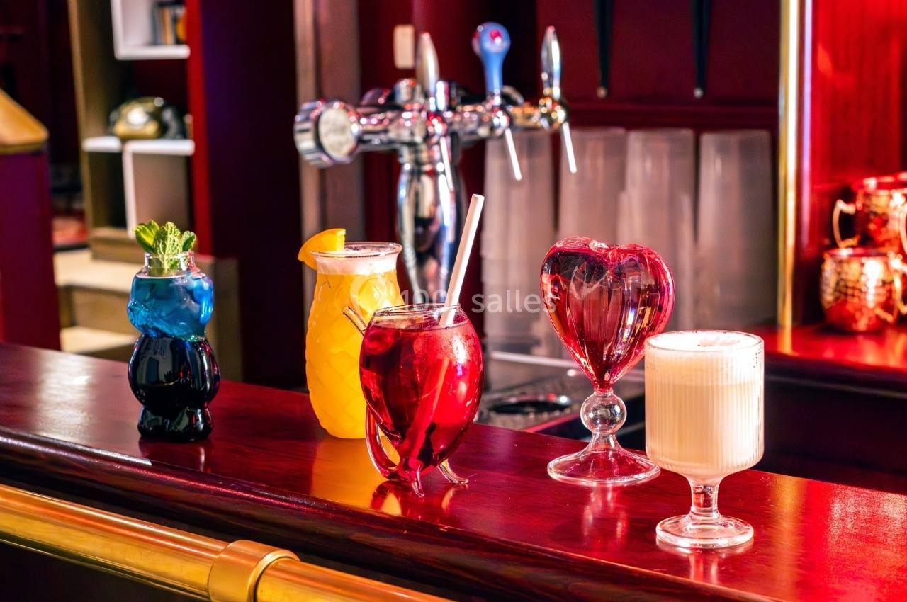 Quatre cocktails colorés servis dans des verres originaux sur un comptoir de bar en bois, avec des tireuses en arrière-plan.