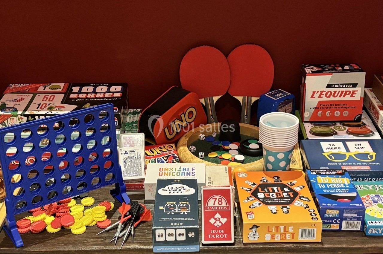 Jeux de société variés, accessoires de jeux de table et échiquier disposés sur une table devant un mur rouge.