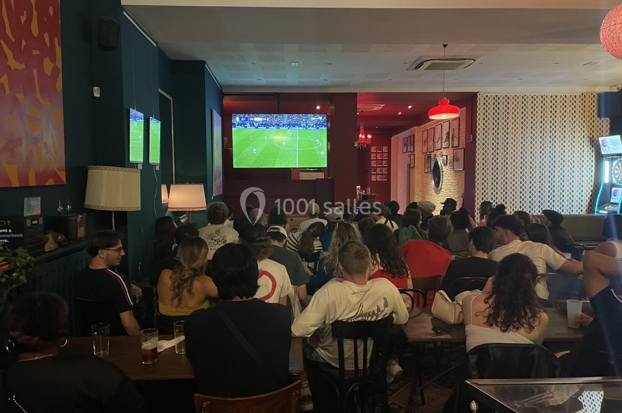 Des personnes assises dans un bar regardent un match de football diffusé sur un écran géant.