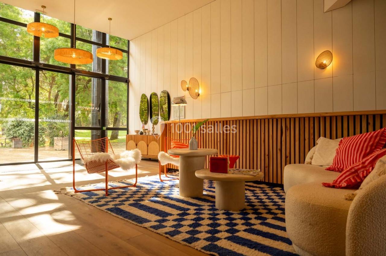 Salon lumineux avec grandes baies vitrées, mobilier moderne, tapis à motifs bleus et blancs, et vue sur un jardin verdoyant.