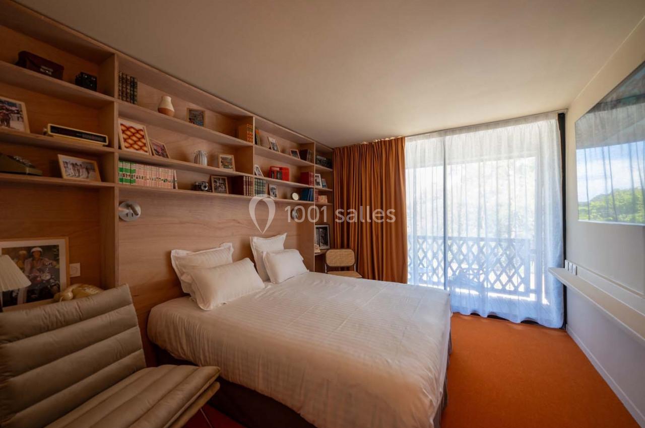 Chambre lumineuse avec lit double, étagères en bois remplies d'objets décoratifs et grande baie vitrée avec rideaux.