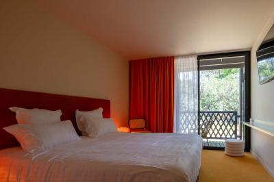 Chambre lumineuse avec lit double, balcon donnant sur un espace arboré, rideaux rouges et lampe de chevet allumée.