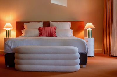 Chambre lumineuse avec lit double, balcon donnant sur un espace arboré, rideaux rouges et lampe de chevet allumée.