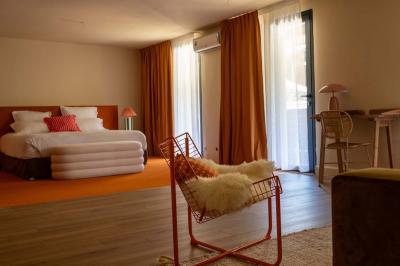 Chambre lumineuse avec lit double, balcon donnant sur un espace arboré, rideaux rouges et lampe de chevet allumée.