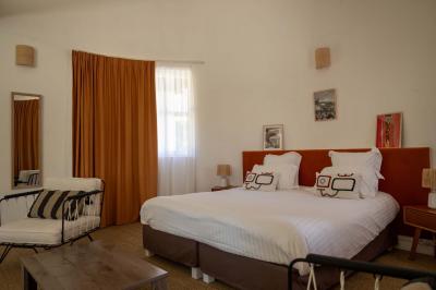 Chambre lumineuse avec lit double, balcon donnant sur un espace arboré, rideaux rouges et lampe de chevet allumée.