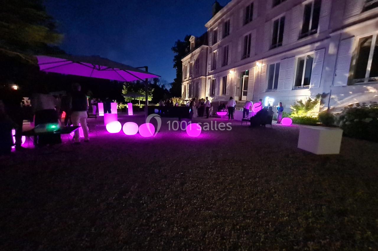 Cour d’un bâtiment éclairé de nuit, avec des sphères lumineuses roses et des invités rassemblés en extérieur.