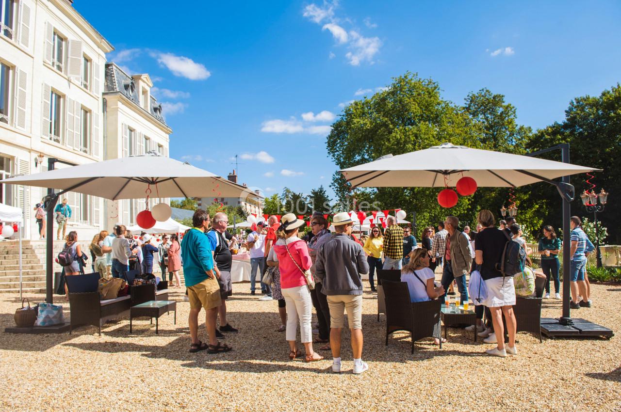 Groupe de personnes discutant et partageant un moment convivial dans un jardin avec parasols par une journée ensoleillée.