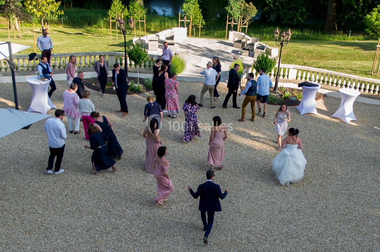 Groupe de personnes dansant en plein air sur une terrasse en gravier, entourée de verdure et de mobilier de jardin.