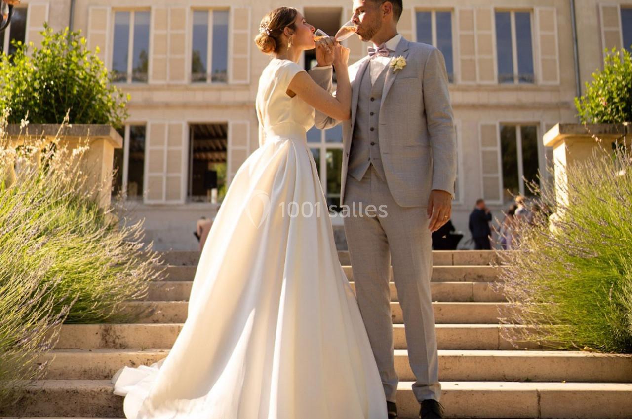 Un couple de mariés échange un toast sur les marches d'un bâtiment élégant sous une lumière ensoleillée.