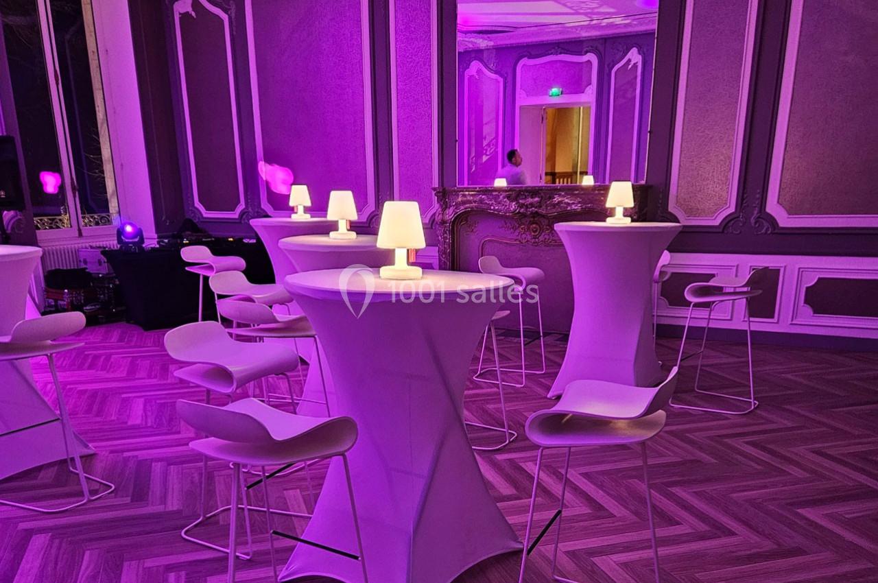 Salle élégante avec tables hautes, chaises design et éclairage violet créant une ambiance tamisée.
