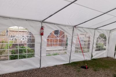 Intérieur d'une tente blanche avec des parois transparentes laissant voir un jardin et une porte en bois.