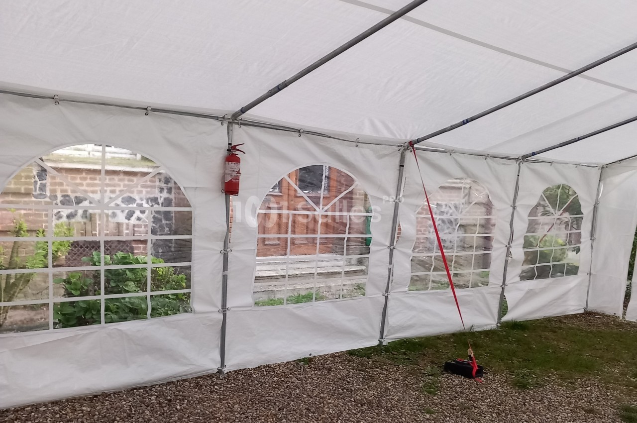 Intérieur d'une tente blanche avec des parois transparentes laissant voir un jardin et une porte en bois.