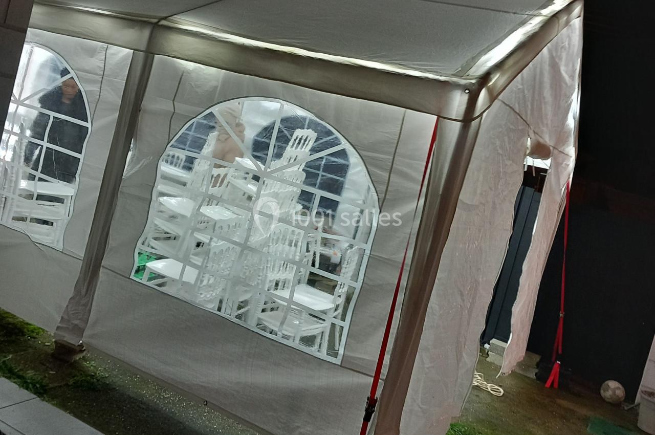 Tente blanche éclairée avec des chaises empilées visibles à travers une fenêtre en plastique transparent.