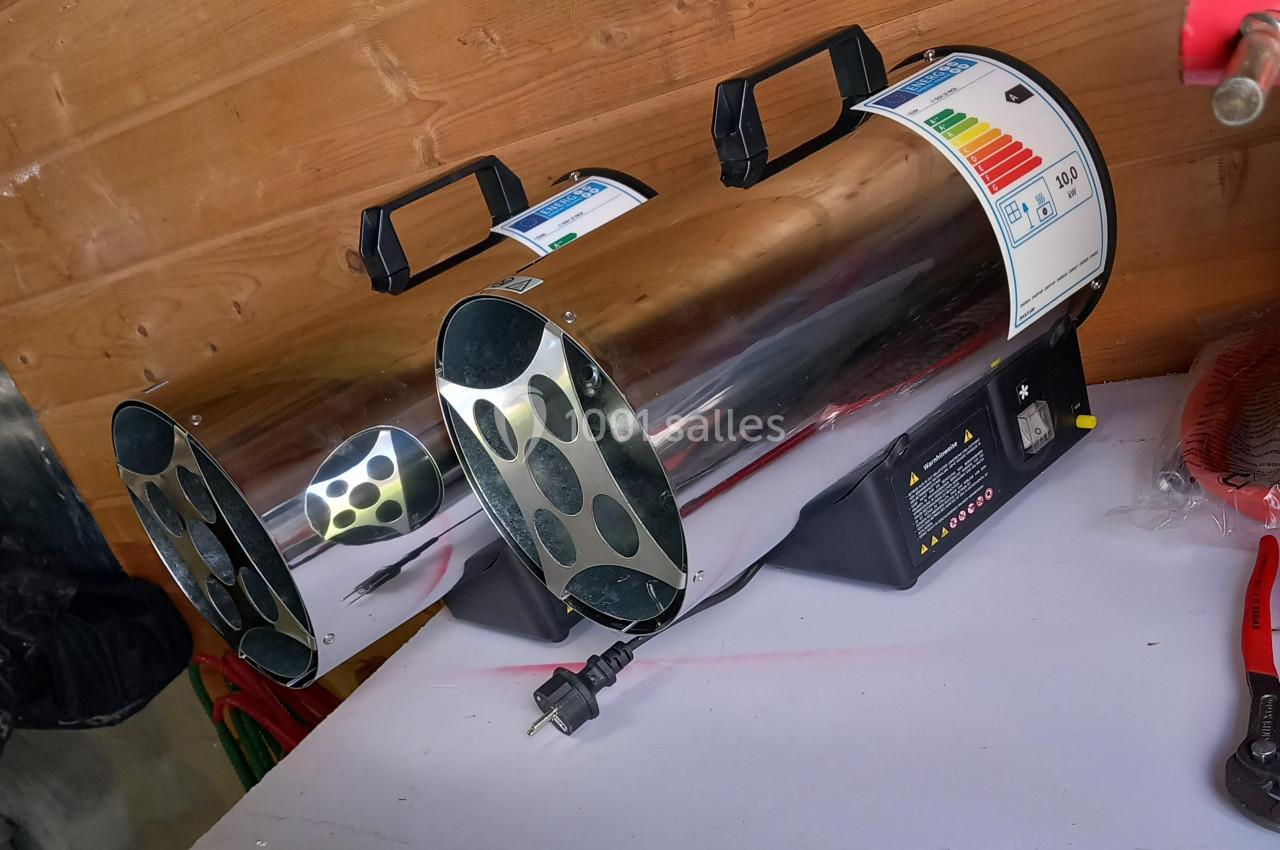 Deux chauffages industriels métalliques posés sur une table blanche, avec un mur en bois en arrière-plan.