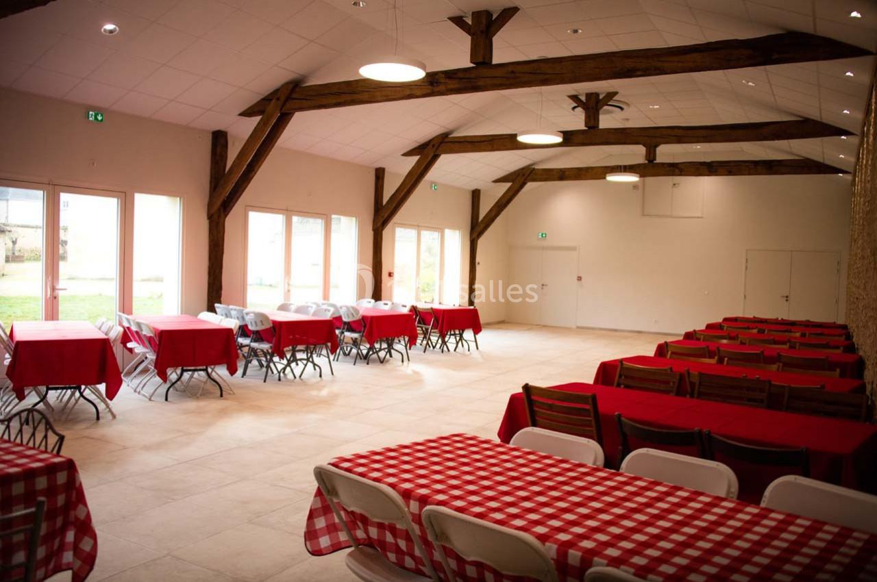 Salle lumineuse avec poutres apparentes, tables rouges et blanches alignées, et grandes baies vitrées donnant sur l…