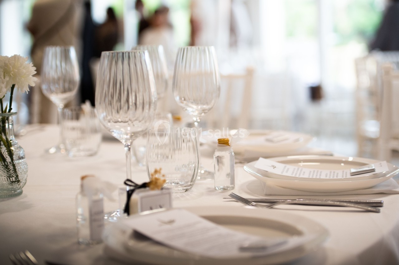 Table dressée avec des assiettes blanches, verres élégants, couverts en métal et petites décorations raffinées.