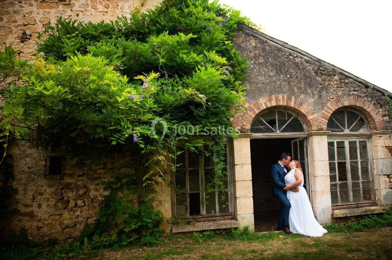 Un couple s'embrasse devant une ancienne bâtisse en pierre partiellement recouverte de verdure.