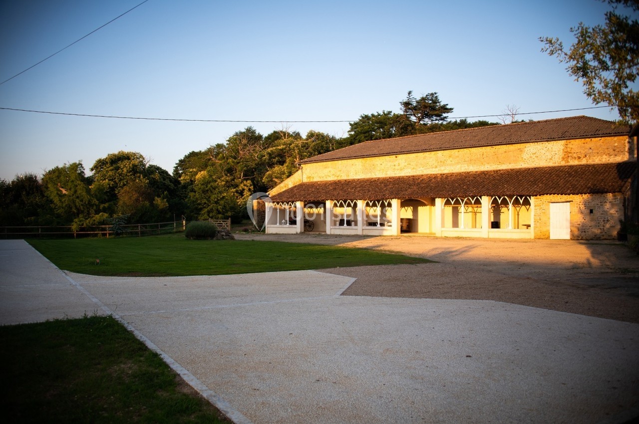 Bâtiment en pierre avec grandes ouvertures, entouré de pelouse et d'arbres, éclairé par une lumière de fin de journée.