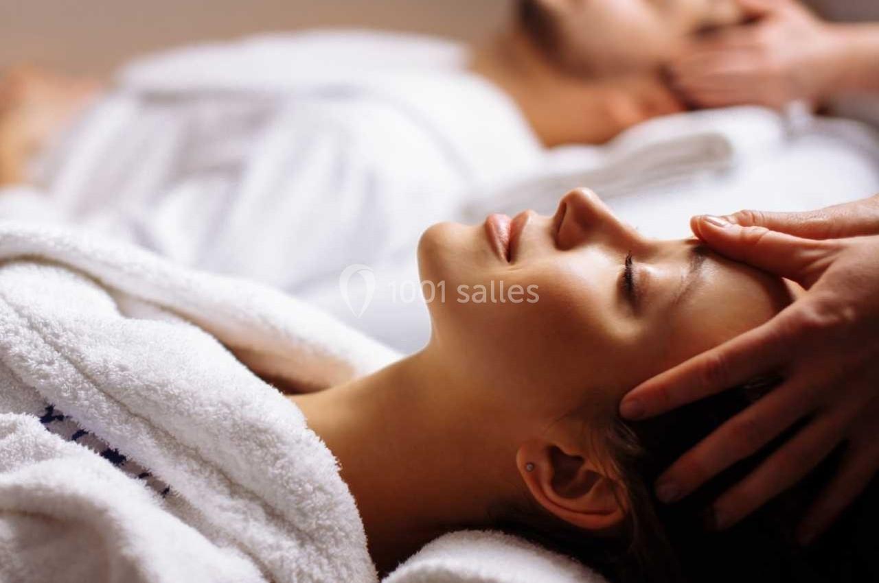 Deux personnes en peignoir blanc reçoivent un massage relaxant de la tête dans un cadre apaisant.