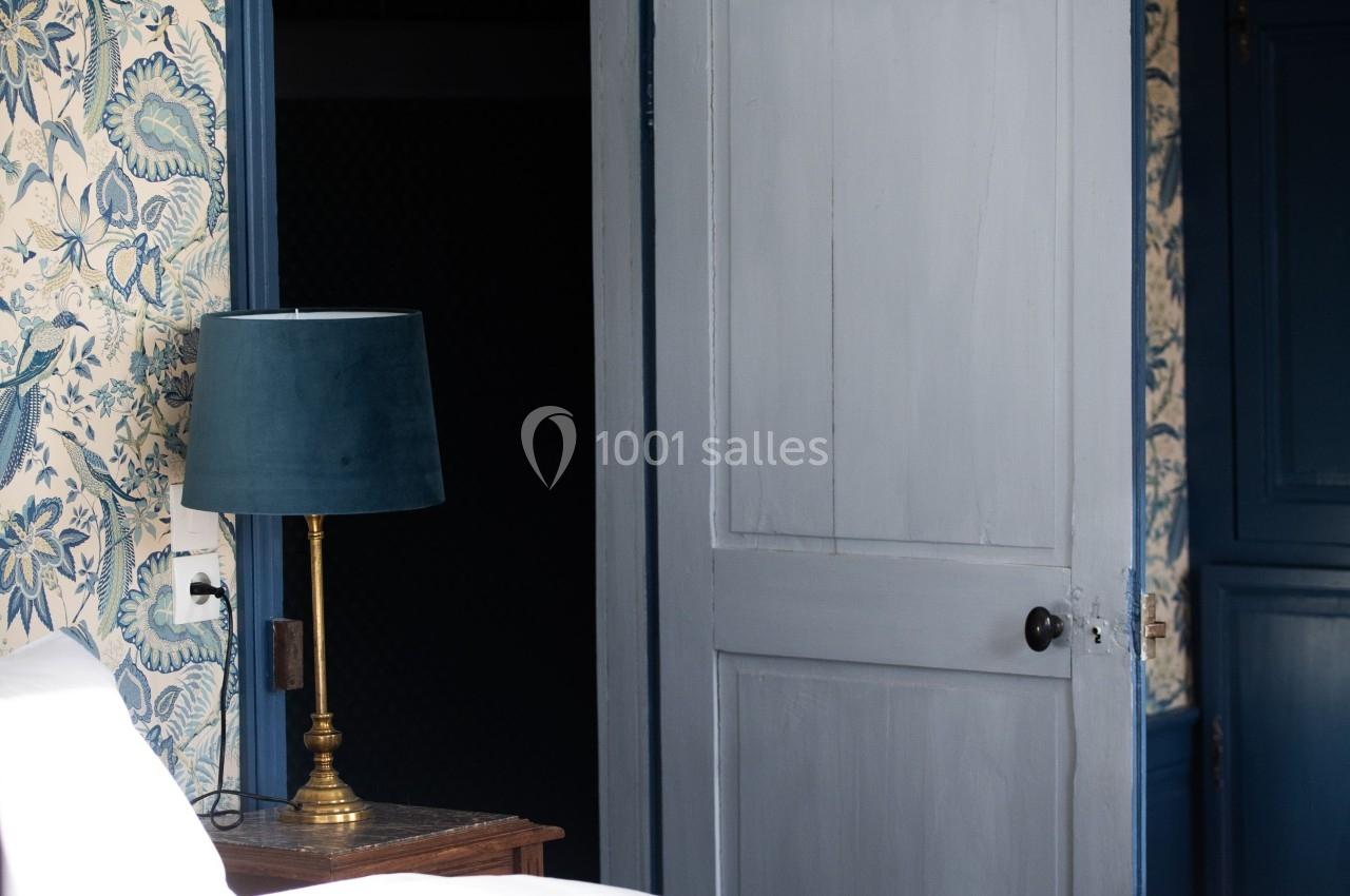 Chambre avec lit, lampe sur table de chevet, mur tapissé à motifs floraux et porte entrouverte.