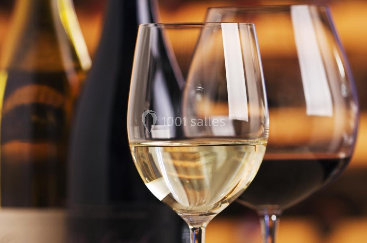 Deux verres de vin, l'un blanc et l'autre rouge, posés devant des bouteilles floues en arrière-plan.