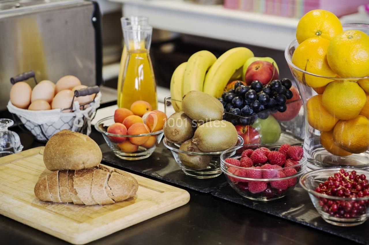 Assortiment de fruits, pain, œufs et jus d'orange disposés sur une table dans un cadre de cuisine.