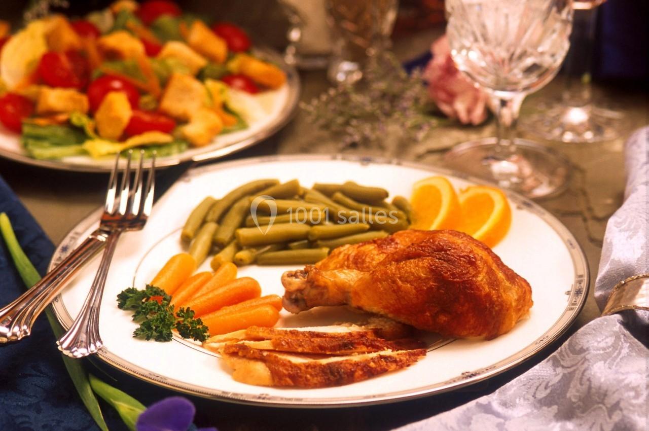 Assiette garnie de poulet rôti, haricots verts, carottes et tranches d'orange, avec une salade en arrière-plan.