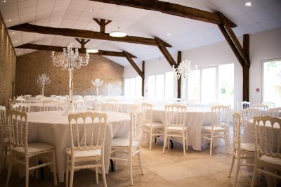 Salle de réception lumineuse avec des tables rondes dressées, des chaises blanches et des chandeliers élégants.