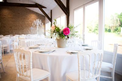 Salle de réception lumineuse avec des tables rondes dressées, des chaises blanches et des chandeliers élégants.