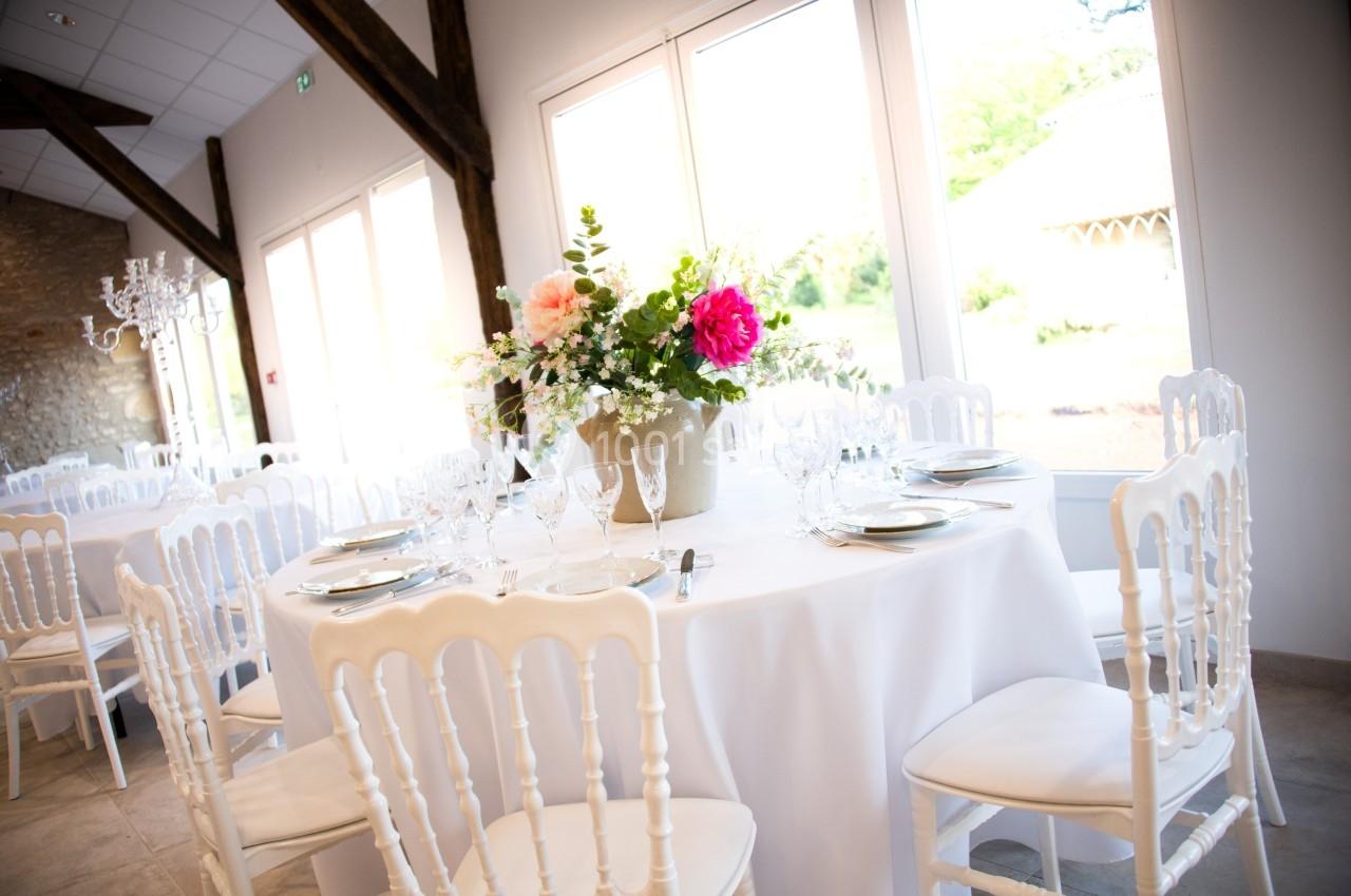 Table ronde décorée avec une nappe blanche, des fleurs colorées et de la vaisselle élégante dans une salle lumineuse.