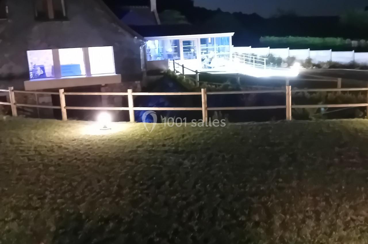 Location salle Saint-Samson-de-la-Roque (Eure) - Manoir Néo Normand #37 Vue nocturne d'un jardin avec une maison éclairée, une clôture en bois, un banc au premier plan et la lune visible.