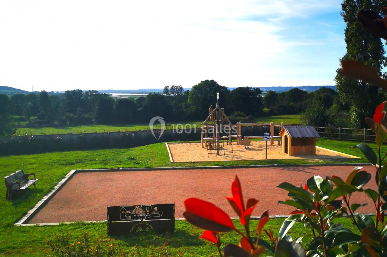 Location salle Saint-Samson-de-la-Roque (Eure) - Manoir Néo Normand #35 Aire de jeux en plein air avec toboggan et cabane, entourée de verdure et éclairée par un ciel ensoleillé.
