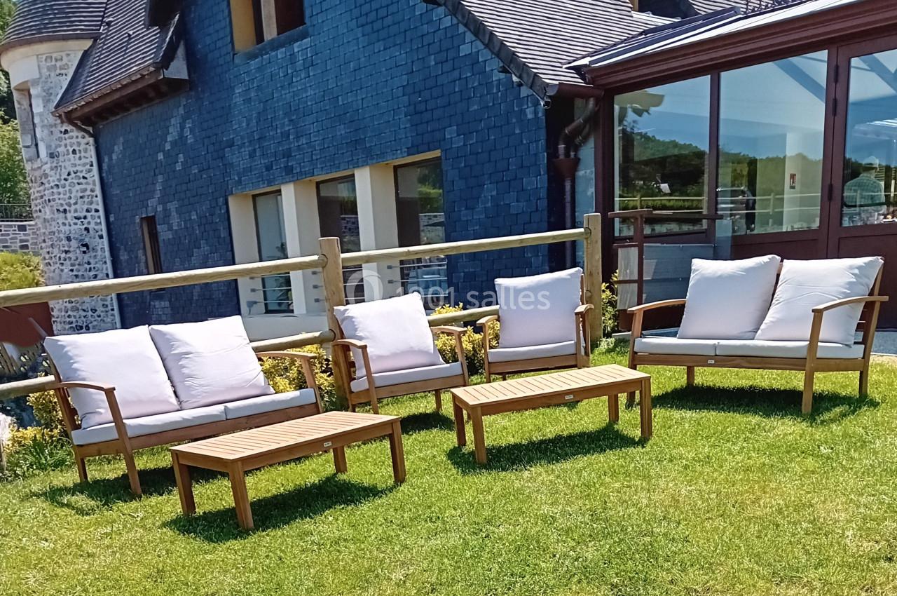 Location salle Saint-Samson-de-la-Roque (Eure) - Manoir Néo Normand #33 Mobilier de jardin en bois avec coussins blancs disposé sur une pelouse devant une maison en ardoise.