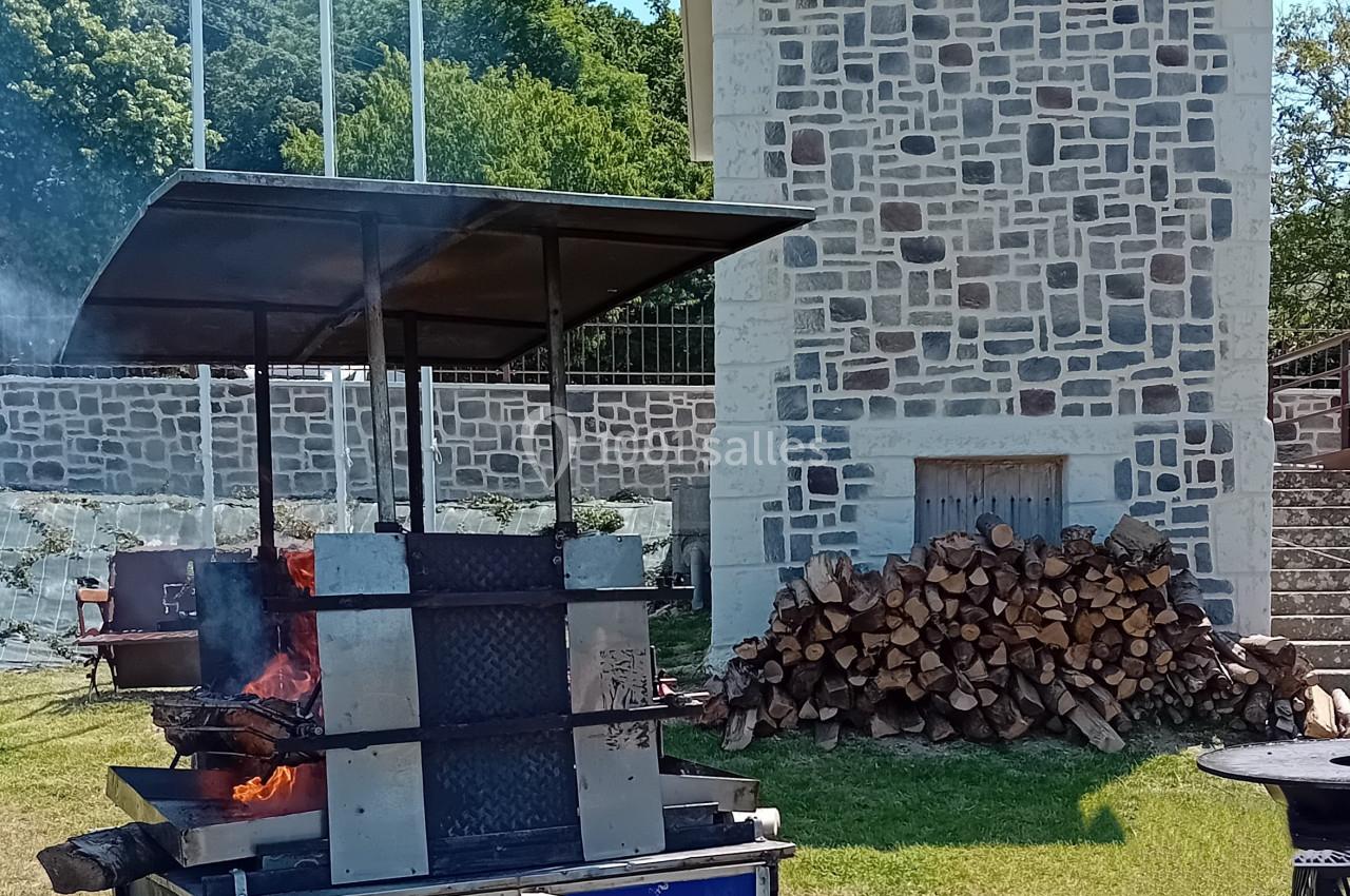 Location salle Saint-Samson-de-la-Roque (Eure) - Manoir Néo Normand #34 Barbecue mobile en métal allumé devant un bâtiment en pierre, avec des drapeaux et un tas de bois à proximité.