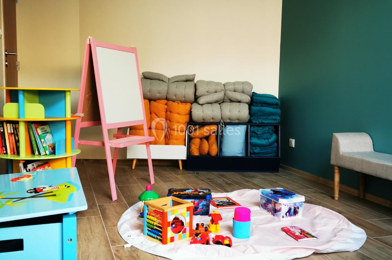 Location salle Saint-Samson-de-la-Roque (Eure) - Manoir Néo Normand #31 Salle de jeux pour enfants avec tapis, jouets, tableau blanc et étagères colorées sur un sol en bois.