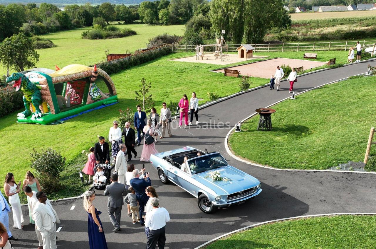 Location salle Saint-Samson-de-la-Roque (Eure) - Manoir Néo Normand #19 Un groupe de personnes rassemblé autour d'une voiture décapotable bleue dans un parc avec une aire de jeux en arrière-plan.