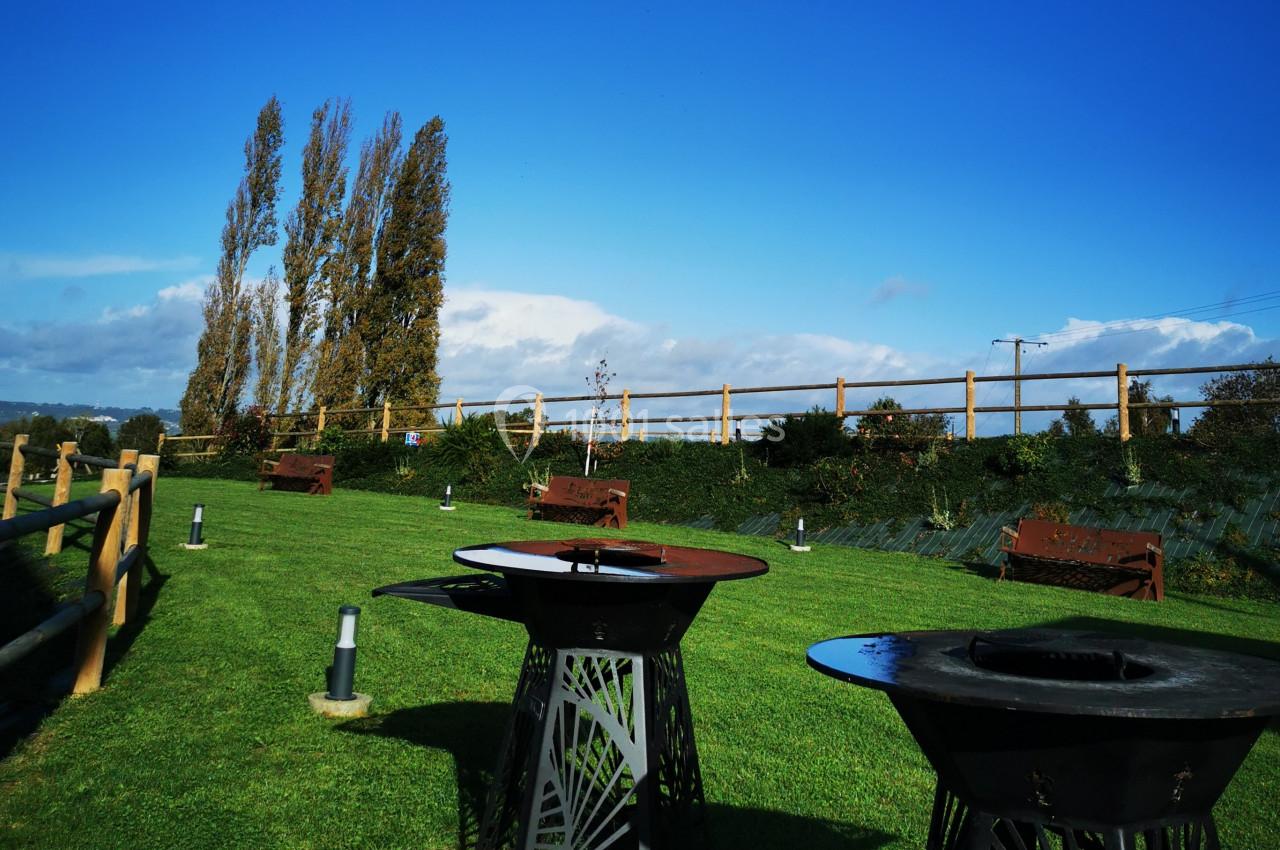 Location salle Saint-Samson-de-la-Roque (Eure) - Manoir Néo Normand #38 Barbecues métalliques sur une pelouse verte avec des bancs en bois, entourés d'arbres et d'une clôture en bois.